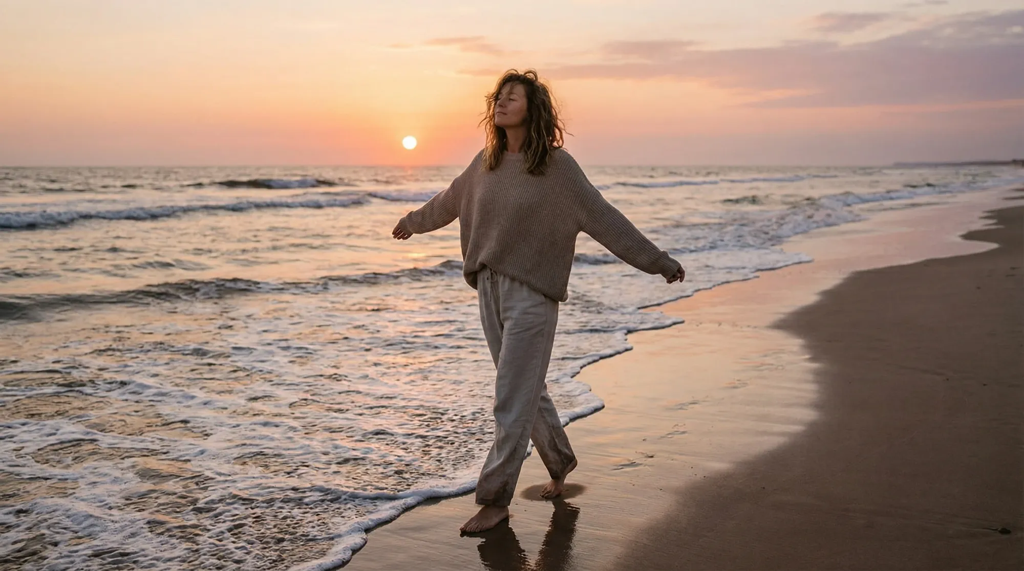 Woman walking barefoot along the beach at sunset