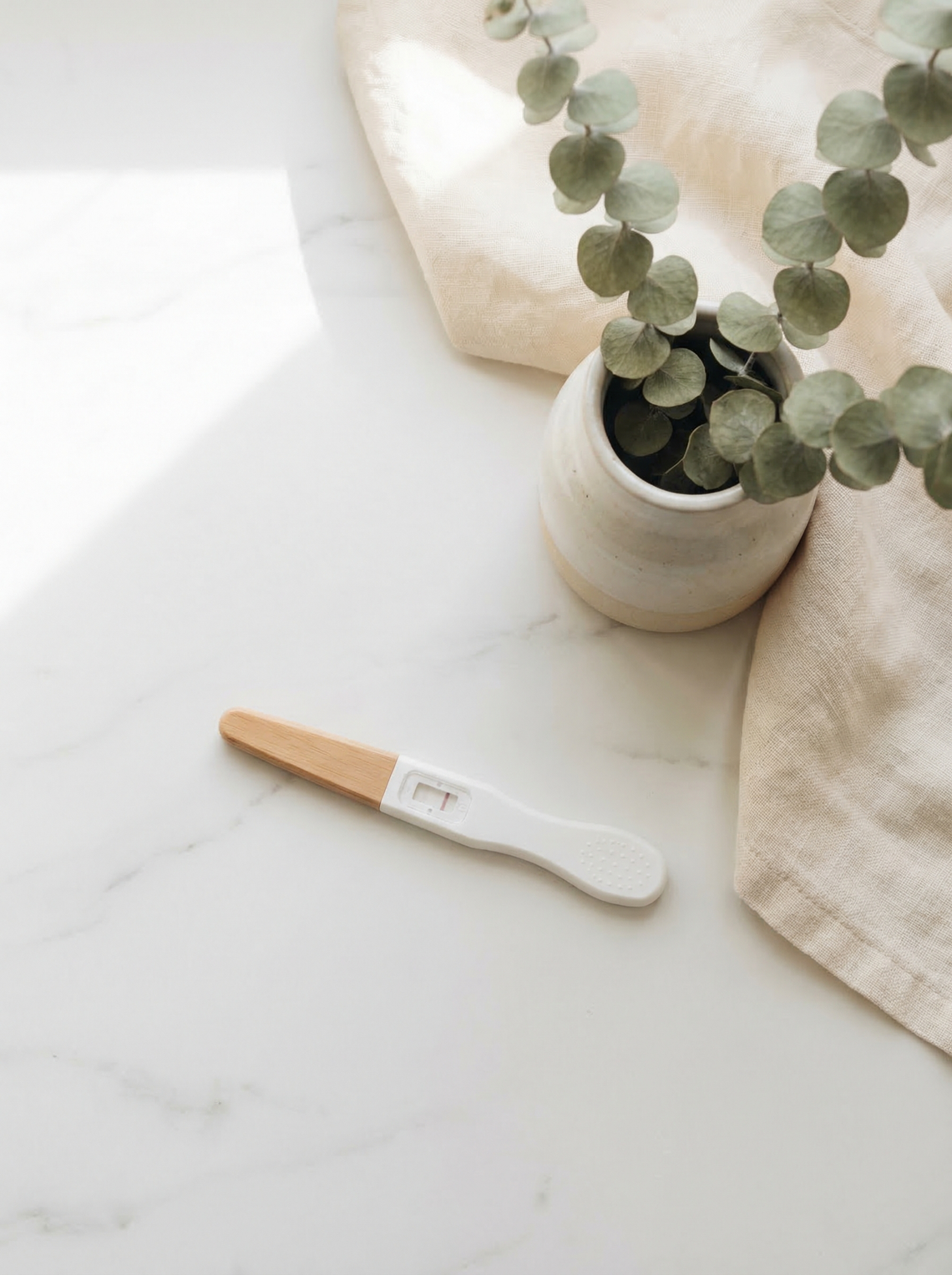 Pregnancy test on marble surface with eucalyptus and linen in natural morning light